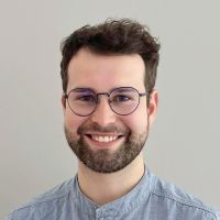 Juraj Zovinec - Developer: Smiling man with curly black hair, short full beard and round black glasses.