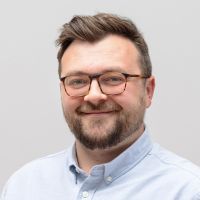 Ben Sandler - Sales Manager: Smiling man with dark brown hair, dark beard and square horn-rimmed glasses.